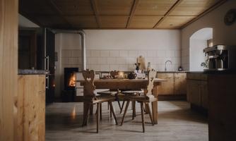 An inviting kitchen with wooden furniture and a large dining table. In the background, a cozy fireplace is burning.