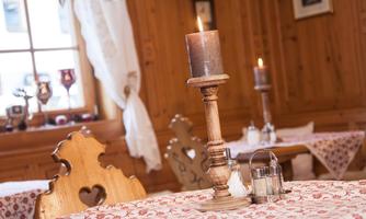 A cozy restaurant with wooden furniture and a table setting. On the table, there is a candle holder with a burning candle and a salt and pepper shaker.