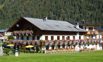 A traditional building with blooming flower boxes and a well-kept garden. In the background, green mountains and trees can be seen.