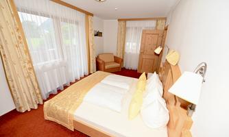 A cozy bedroom with a double bed and an armchair. Large windows let in plenty of daylight and create a bright atmosphere.