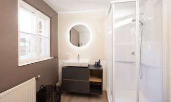 A modern bathroom with a shower and a large round mirror. The walls are painted in neutral tones and there is a stylish sink.