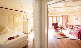 An elegant room with a large bed and a cozy seating area. The space has plenty of daylight and a warm, inviting atmosphere.