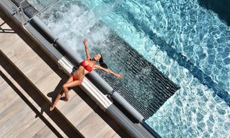 A woman in a red bikini relaxes at the edge of a swimming pool. The water is clear and invites swimming.