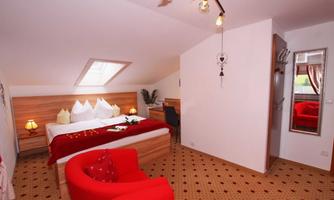 A cozy bedroom with a large bed and red accents. The walls are bright, and there is a mirror as well as a small seating area.