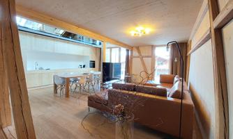 A modern living and dining room with wood paneling. There is a cozy couch, a dining table, and an open kitchen.