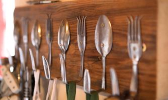 A rustic wooden board with various spoons and forks neatly hanging. The utensils are made of metal and give the kitchen a charming look.