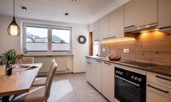 A modern kitchen with a dining table and stylish chairs. Bright furniture and large windows create a friendly atmosphere.