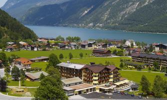A picturesque landscape with a clear lake and green meadows. In the foreground are several cozy buildings, and the mountains in the background provide an impressive backdrop.