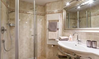 A modern bathroom with a shower and a sink. The walls are elegantly tiled and a large mirror creates a bright atmosphere.
