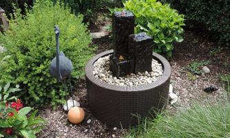 A beautiful garden area with a waterfall and decorative stones. In the background, lush plants and a stylized stork can be seen.