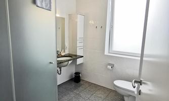 A modern bathroom with gray tiles and a glass shower area. There is also a sink with a mirror and a window for natural light.