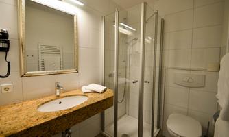 A modern bathroom with a shower and a granite sink. The walls are brightly tiled, and the room design is simple and functional.