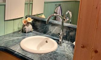 A modern sink with an elegant faucet stands on a marbled countertop. In the background, decorative elements and wall coverings in soft colors can be seen.