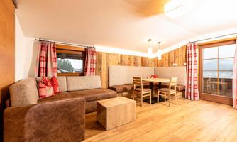 A modern living room with a cozy sofa and a wooden table. Large windows offer a view outside and let in plenty of light.