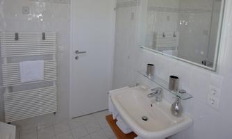A modern bathroom with a sink and a large mirror. White tiles and fresh towels create a bright, clean atmosphere.