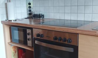 A modern kitchen with wooden surfaces and white tiles. There is a stove, an oven, and a microwave.