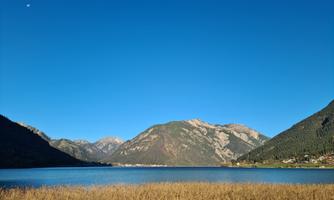 A tranquil lake surrounded by high mountains. The sky is clear and blue, creating a peaceful atmosphere.