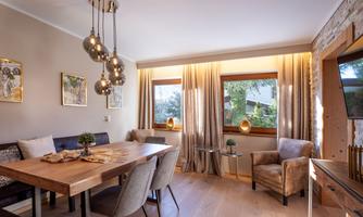 A modern living room with a large wooden table and stylish chairs. Bright windows create a pleasant light atmosphere.