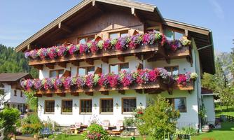 A charming countryside-style house with blooming balcony boxes and a well-kept garden. The stunning backdrop of the mountains enhances the idyllic atmosphere.