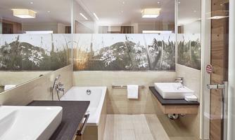 A modern bathroom with an elegant sink and a bathtub. The walls are designed with a decorative glass wall and natural motifs.