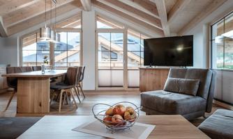 A modern living room with wooden ceilings and large windows. A dining table and a cozy couch create an inviting atmosphere.