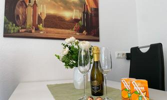 An elegant table with a bottle of sparkling wine, two glasses, and snacks. In the background, wine barrels and a landscape with vineyards can be seen.