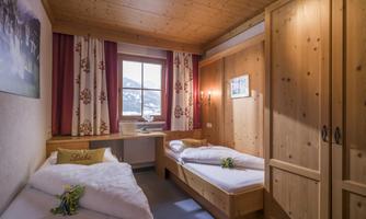 A cozy bedroom with two single beds and wooden furniture. Large windows offer a view of the mountains.