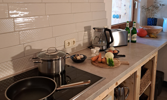 A modern kitchen with a stove, pots, and fresh vegetables. There are also drinks and a bowl of fruit on the counter.