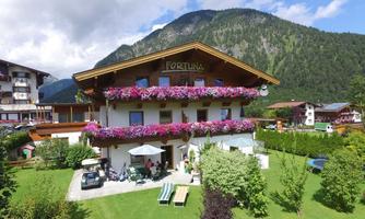 A charming mountain house with colorful flowers on the balcony. Surrounded by green lawn and mountains in the background.