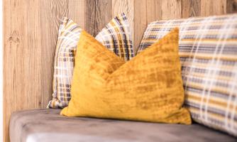 A modern sofa with cushions in front of a wooden wall. The cushions have different patterns and colors, including a striking yellow cushion.