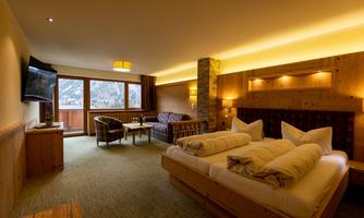 A cozy hotel room with wooden decor and a large window that lets in plenty of light. There is a double bed, a television, and a comfortable seating area.
