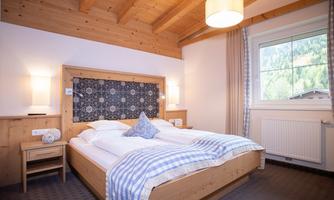 A cozy bedroom with a double bed and wood paneling. The window offers a view of nature.