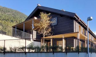 A modern wooden house with a beautiful facade. In the background, green mountains can be seen.