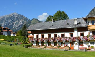 A picturesque house in the mountains with many flowers on the balconies. The surroundings are green and the landscape is surrounded by majestic mountains.