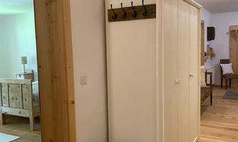 A bright hallway with a white cabinet and a coat rack. Visible are hardwood floors and a warm, cozy atmosphere.