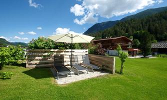 A quiet garden with loungers and a sun umbrella. In the background, mountains and cozy cabins can be seen.