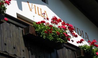 A sunny building with the inscription "VILLA" and many red flowers. The facade is made of wood, giving it a cozy atmosphere.