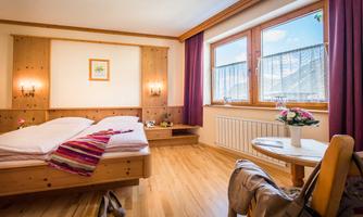 A cozy bedroom with wood paneling and two beds.  
Large windows provide a view and plenty of daylight, as well as a small table with flowers.