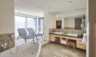 A modern bathroom with a large bathtub and a double sink. Large windows provide plenty of natural light and a view outside.
