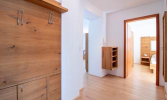A bright hallway with wooden paneling and modern furniture. Additional rooms are visible in the background.