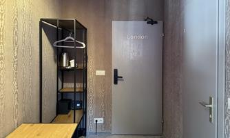 A modern room with a door labeled "London." There is a shelf, a table, and a chair, as well as an electric kettle on an open shelf.