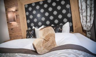 A cozy bedroom with a large bed and a heart-shaped wooden decoration. The background is designed with an elegant pattern and warm light sources.