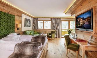 A cozy hotel room with a double bed and modern wooden design. Large windows offer a view of the surroundings, and there is a seating area with a desk.
