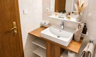 A modern bathroom with a wooden washstand and a white sink. On the shelf are care products and decorative elements like dried flowers.
