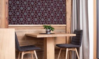 A modern dining area with a wooden tray and two dining chairs. The wall is decorated with an elegant, graphic pattern.
