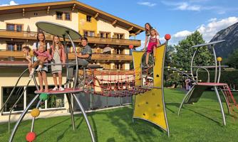 A playground with children playing on a modern climbing frame. In the background, a beautiful building and a green meadow can be seen.