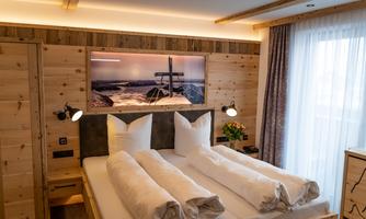 A modern bedroom with wooden interior and two beds. A picture of a coastal landscape hangs on the wall.