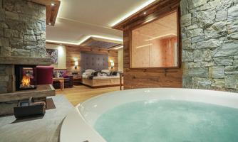 An elegant room with a hot tub and a cozy fireplace. The walls are made of stone, which gives the space a rustic atmosphere.