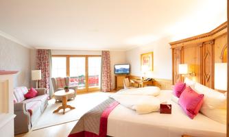 A cozy hotel room with two beds and a light color scheme. There is a living area with a table and two chairs, as well as a large window overlooking the outside.
