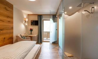 A modern room with a comfortable bed and an adjoining bathroom. Large windows provide plenty of daylight and a homely atmosphere.